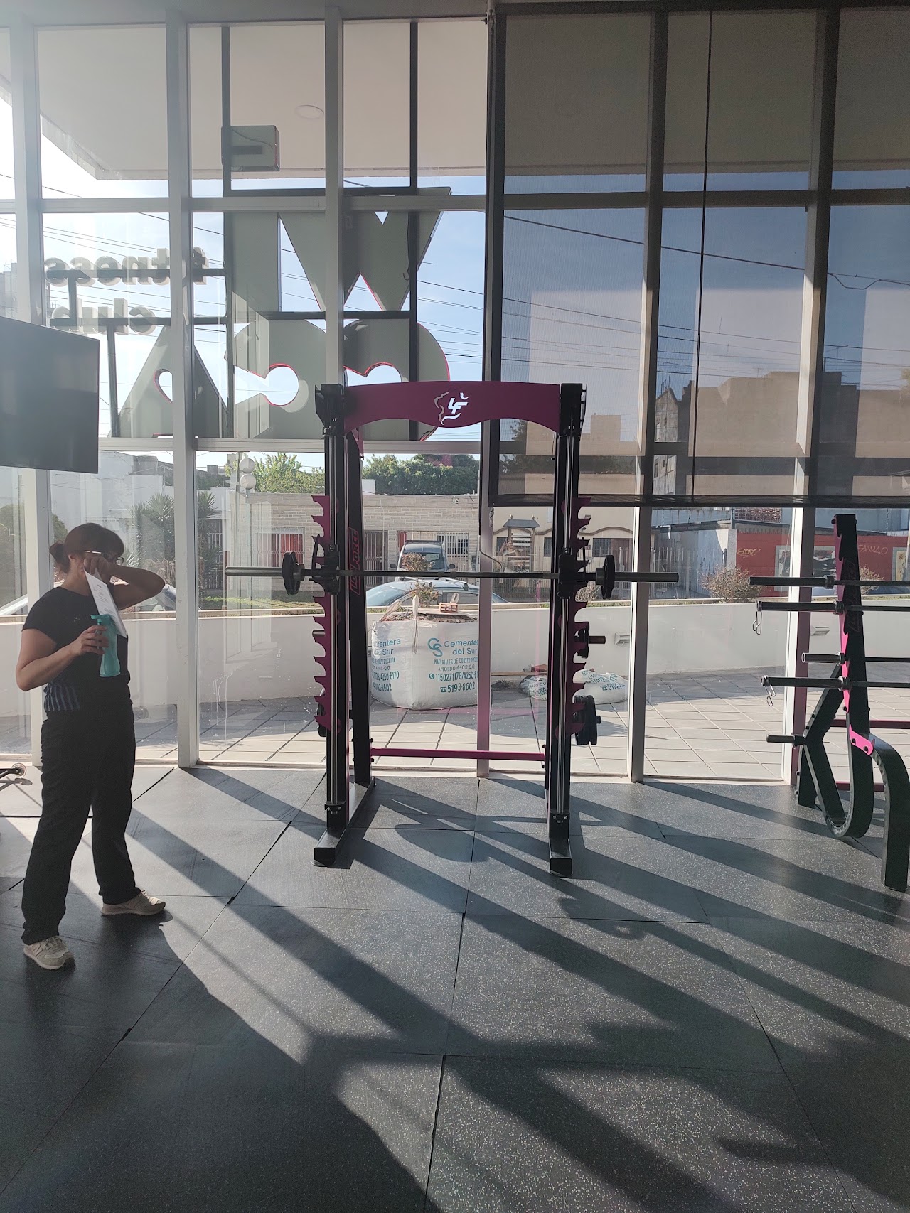 Modern boutique gym interior with custom vibrant magenta pink and matte black weightlifting equipment, dumbbells rack, clean polished dark flooring, bright panoramic floor-to-ceiling glass windows with natural morning light, neon ambient pink light accent, upscale gym in Argentina, professional photography, architectural interior shot, 8k resolution