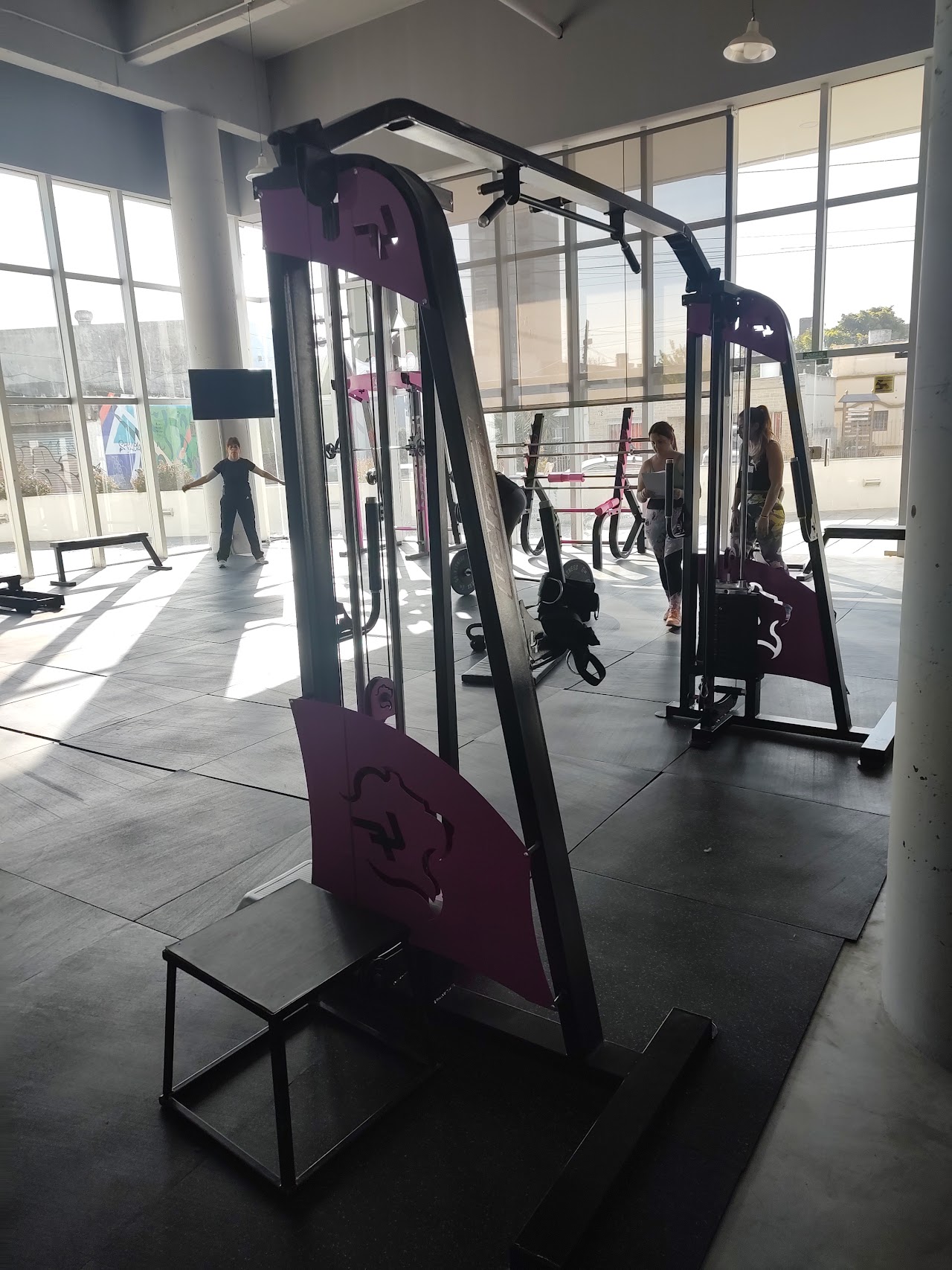 Modern hip thrust bench and barbell station with pink plates and black bench in a boutique fitness club, clean athletic atmosphere, natural window lighting